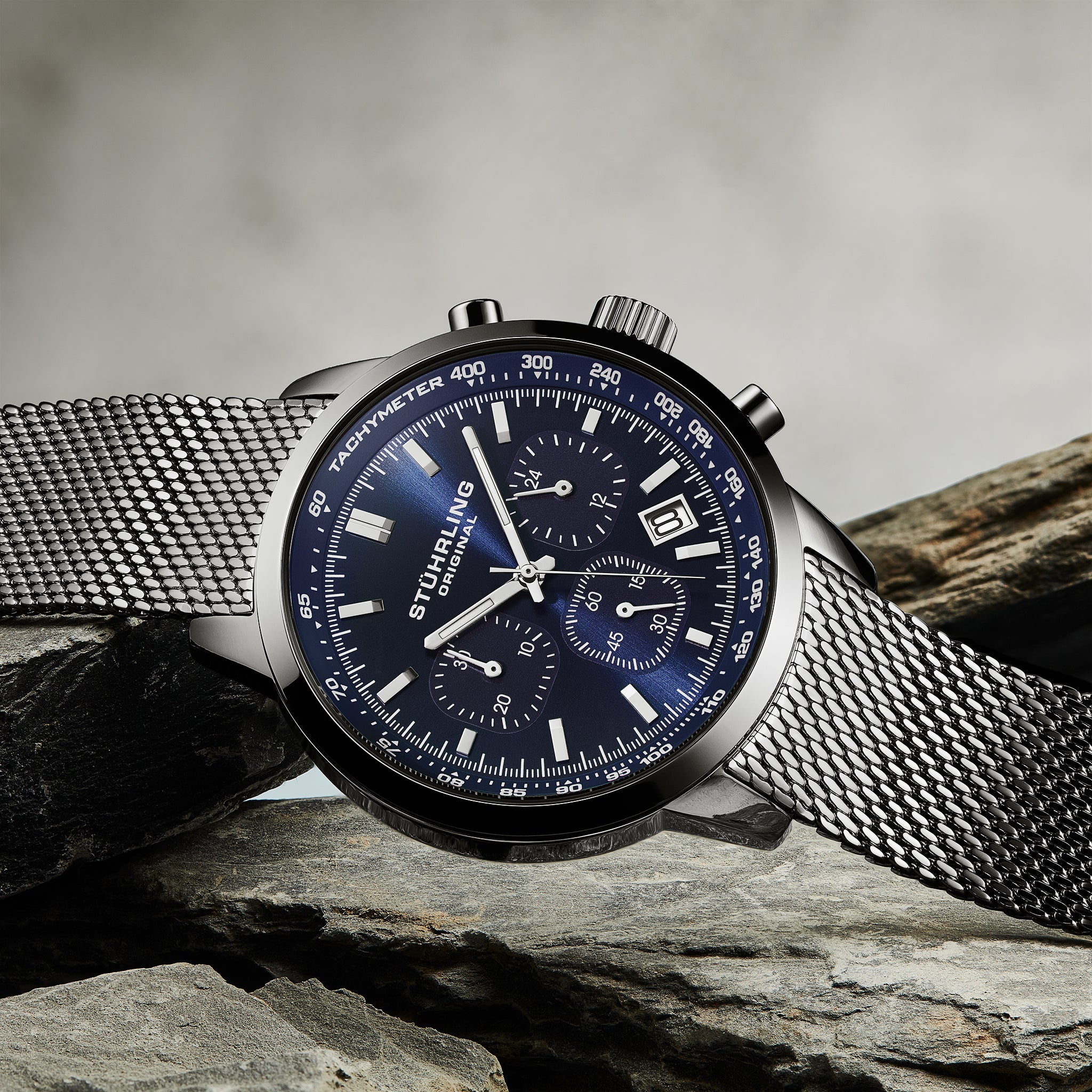 Stuhrling watch with blue face and silver mesh band on a stone surface